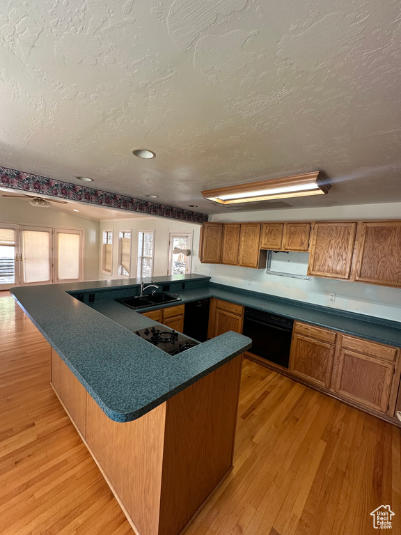 Kitchen with a textured ceiling, brown cabinetry, light wood-type flooring, dark countertops, and a peninsula