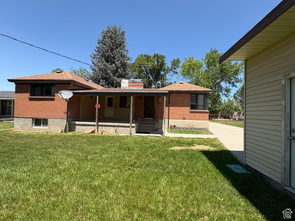 Rear view of house with brick siding, a porch, a yard, roof with shingles, and a chimney