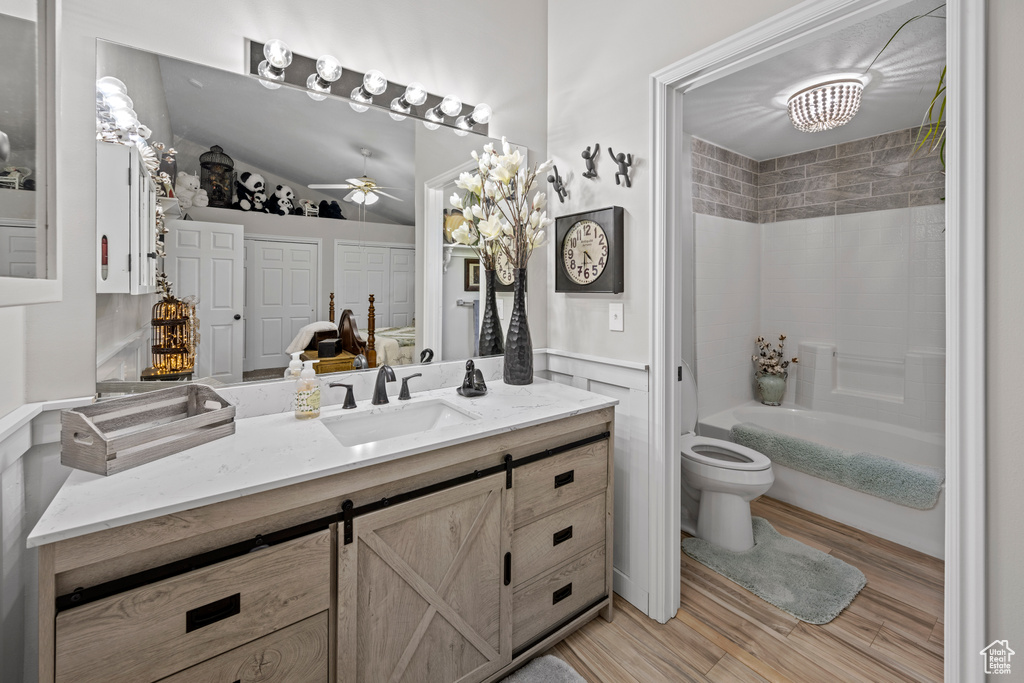 Bathroom featuring vanity, wood finished floors, ceiling fan,  shower combination, and a wainscoted wall