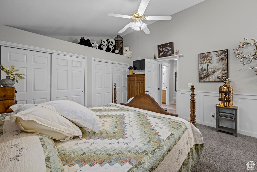 Bedroom with two closets, light carpet, a wainscoted wall, a ceiling fan, and high vaulted ceiling
