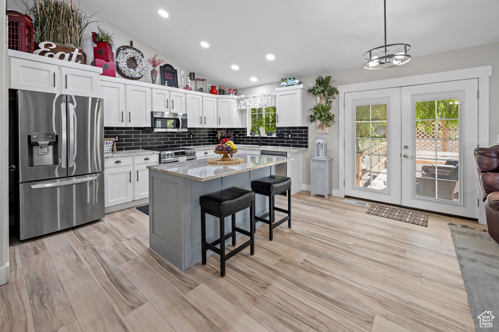 Kitchen featuring appliances with stainless steel finishes, french doors, white cabinetry, tasteful backsplash, and a breakfast bar area
