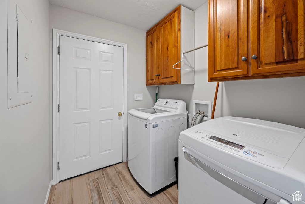 Laundry room featuring cabinet space, washing machine and clothes dryer, light wood-type flooring, and electric panel