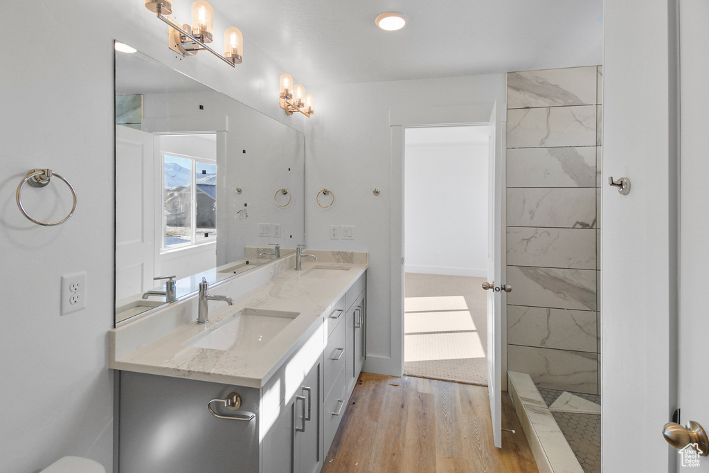 Bathroom featuring double vanity, wood finished floors, a chandelier, and a shower
