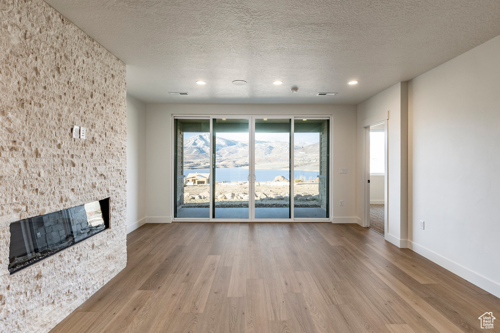 Unfurnished living room with wood finished floors, a fireplace, healthy amount of natural light, recessed lighting, and a textured ceiling