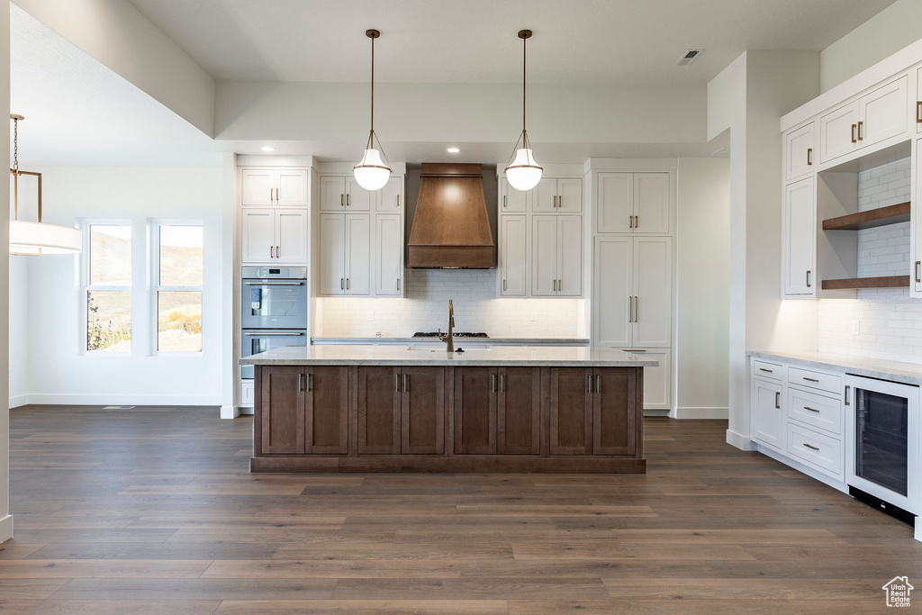 Kitchen featuring custom range hood, wine cooler, appliances with stainless steel finishes, open shelves, and light countertops