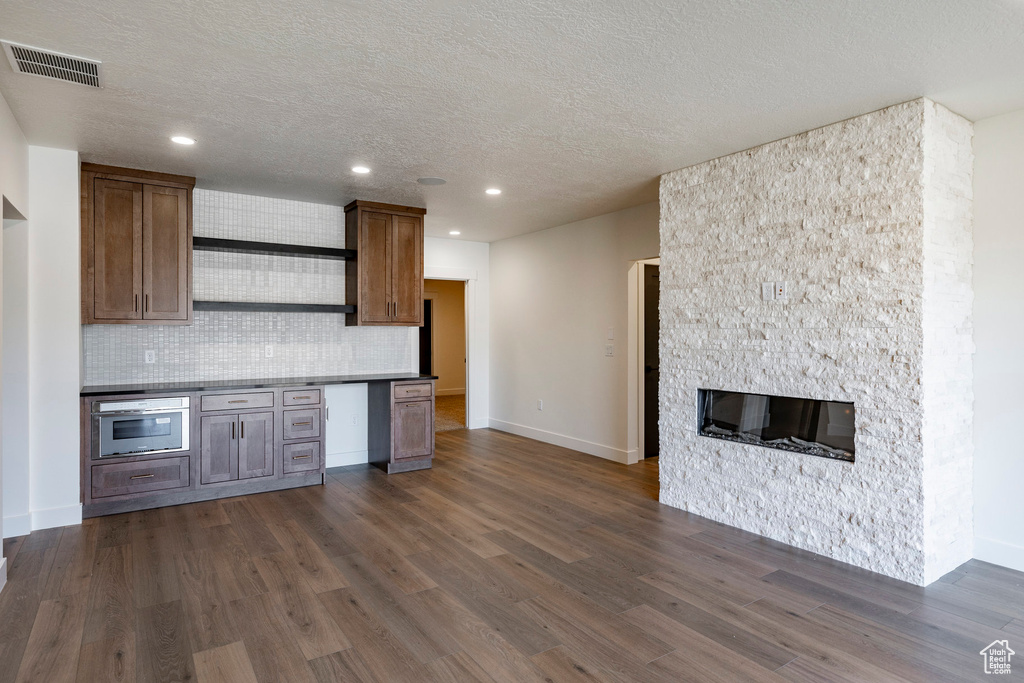 Kitchen with backsplash, a textured ceiling, dark wood-style flooring, a fireplace, and recessed lighting