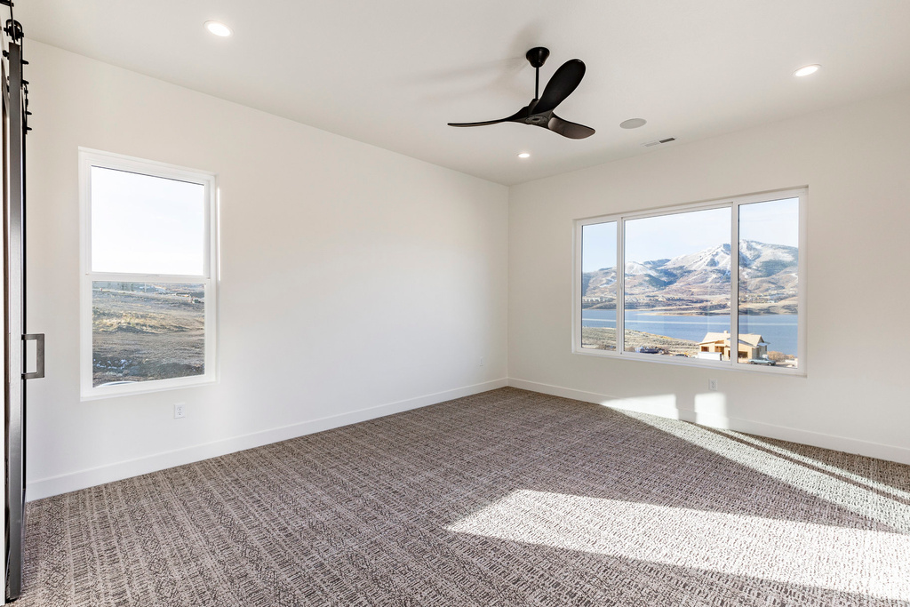 Unfurnished room featuring carpet floors, ceiling fan, recessed lighting, and a water view