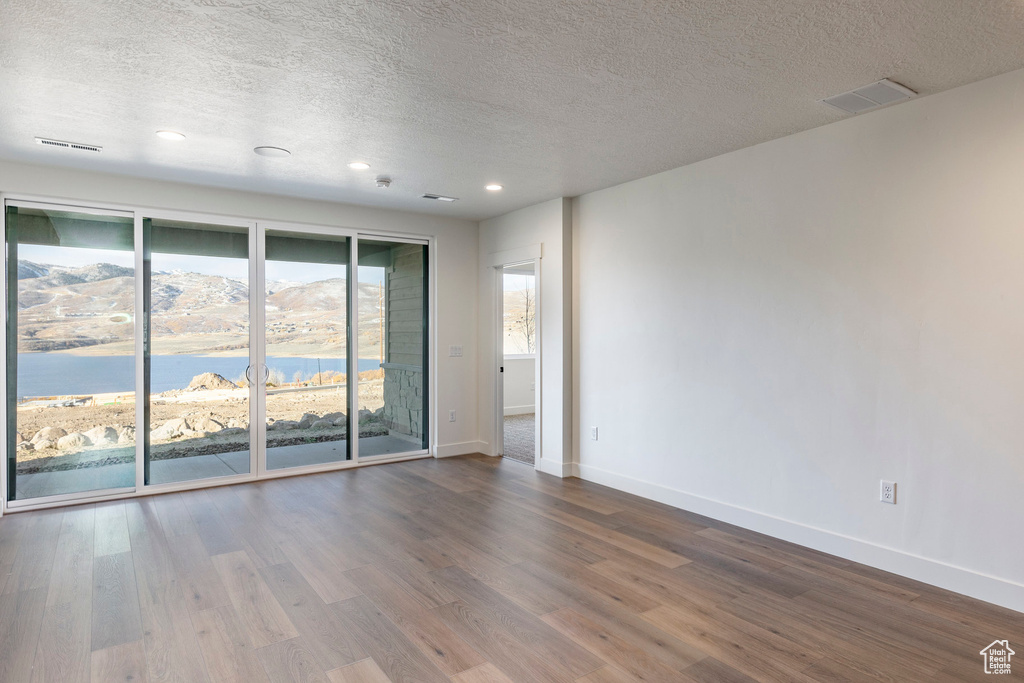 Empty room with a textured ceiling, dark wood-style flooring, recessed lighting, and a water view