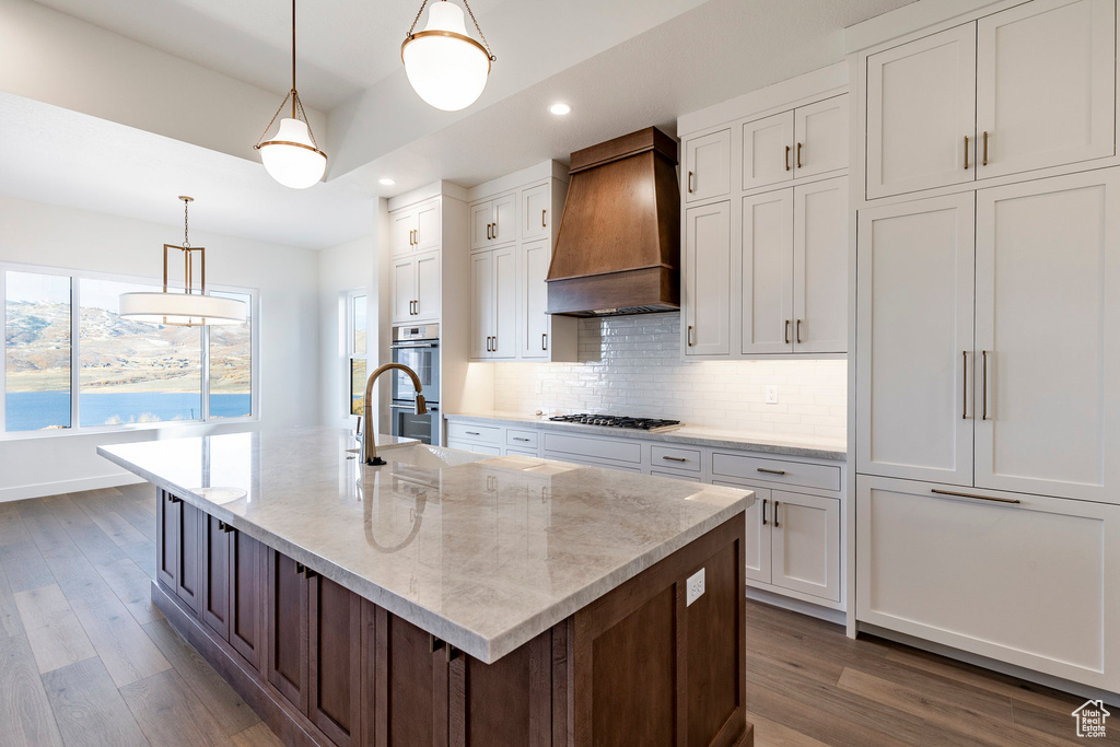 Kitchen with custom range hood, recessed lighting, double oven, wood finished floors, and white cabinetry