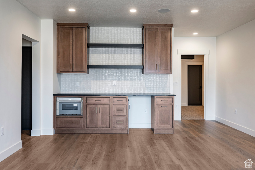 Kitchen with stainless steel oven, wood finished floors, tasteful backsplash, recessed lighting, and dark countertops