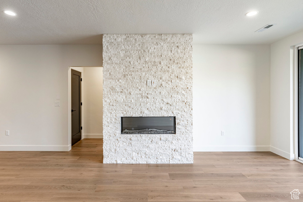 Unfurnished living room featuring a stone fireplace, recessed lighting, light wood-style flooring, and a textured ceiling