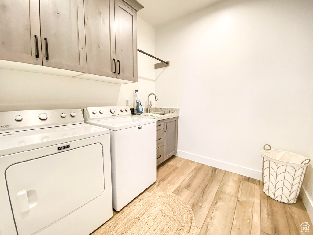 Laundry area with cabinet space, independent washer and dryer, and light wood-style flooring