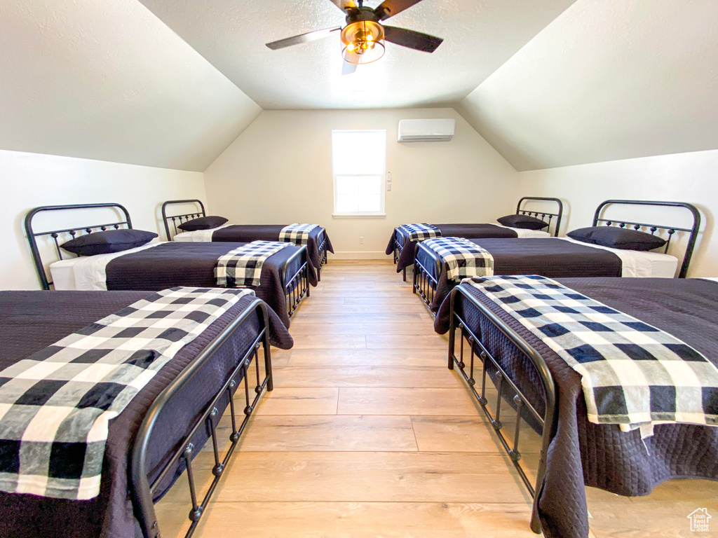 Bedroom with a wall mounted air conditioner, light wood-type flooring, lofted ceiling, and ceiling fan