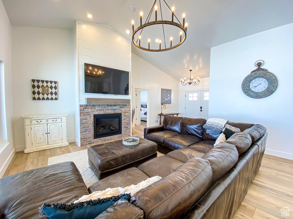 Living room with a chandelier, light wood-style flooring, high vaulted ceiling, a brick fireplace, and recessed lighting