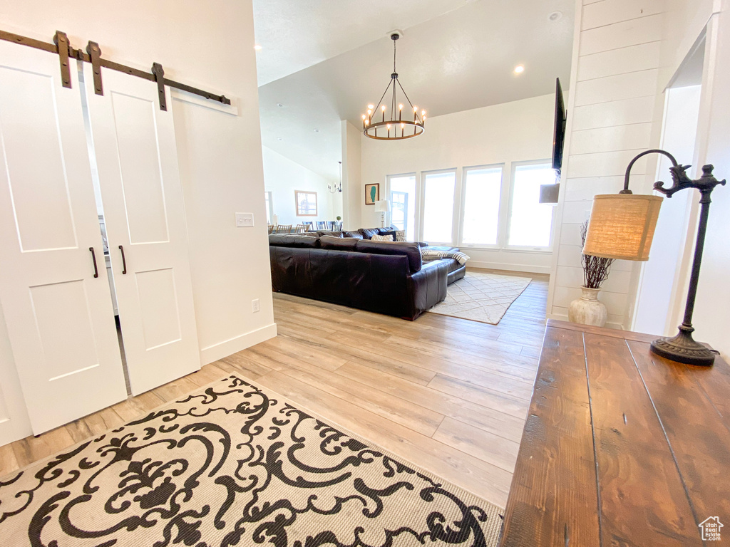 Foyer entrance with a barn door, wood finished floors, vaulted ceiling, and a chandelier