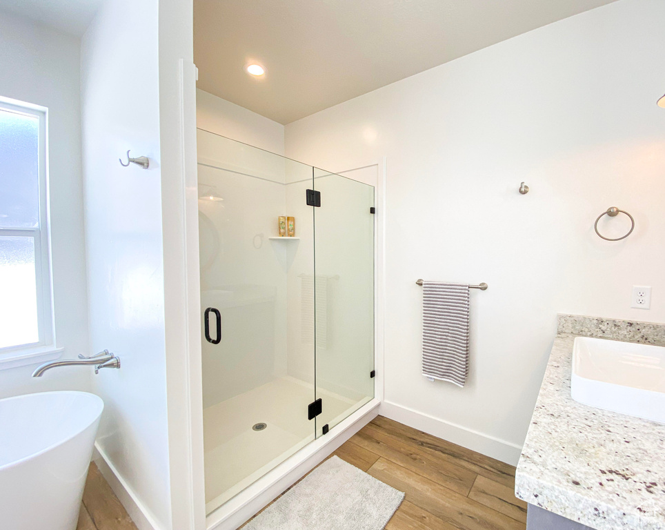 Bathroom featuring a stall shower, vanity, a freestanding tub, wood finished floors, and plenty of natural light