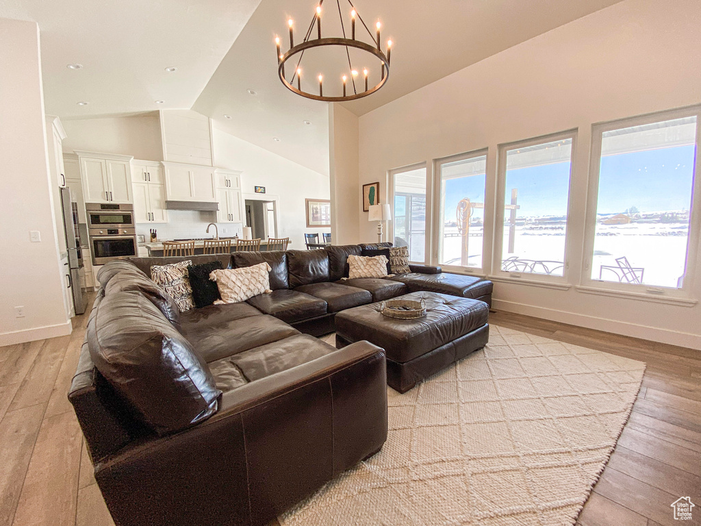 Living room with light wood-style floors, a chandelier, and high vaulted ceiling