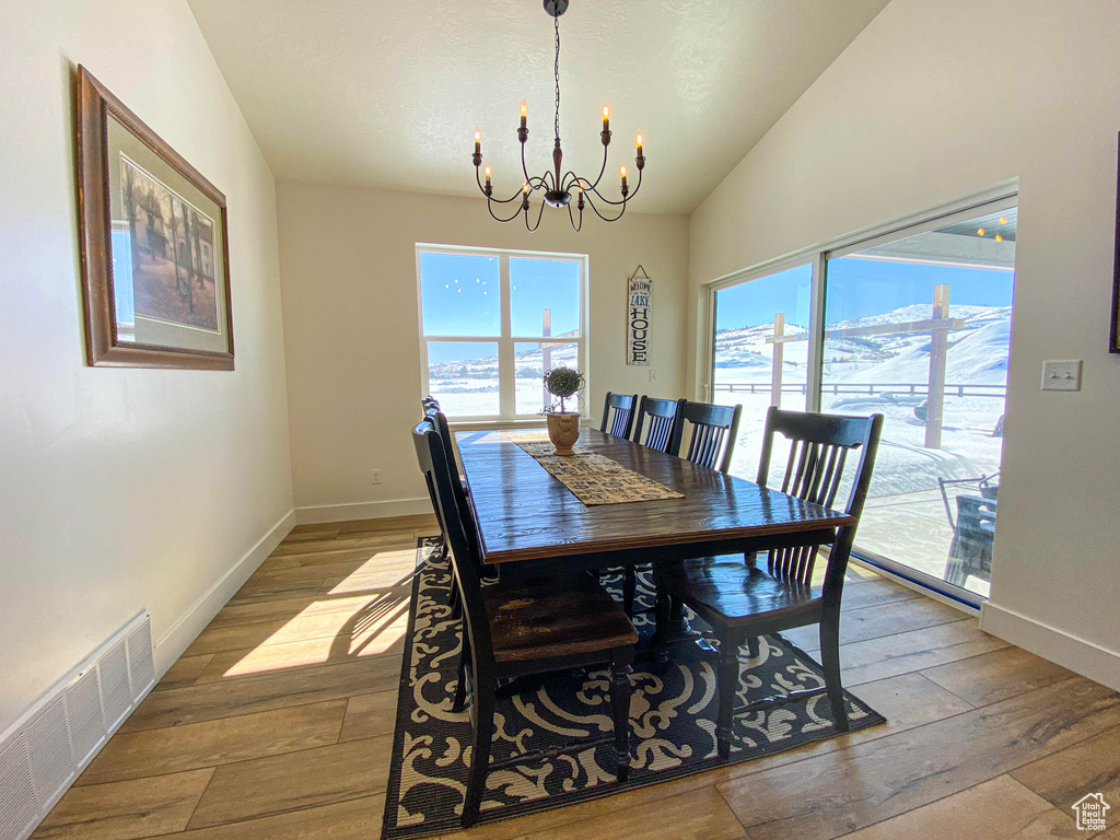 Dining space featuring a chandelier, plenty of natural light, wood-type flooring, and vaulted ceiling