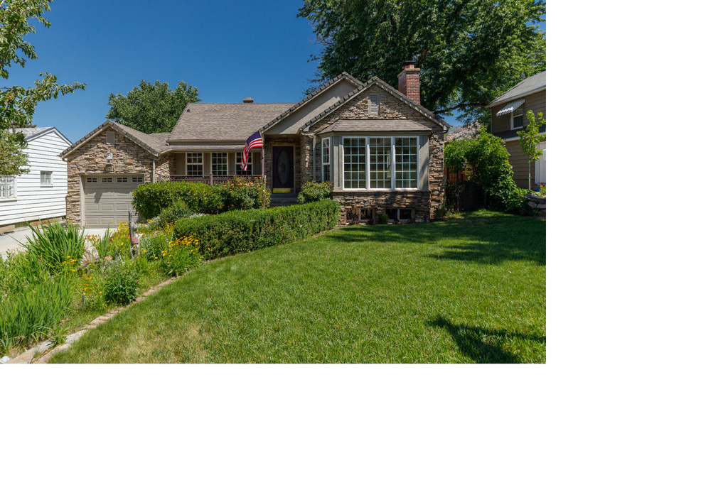 Ranch-style home featuring stone siding, a garage, a front lawn, and a chimney