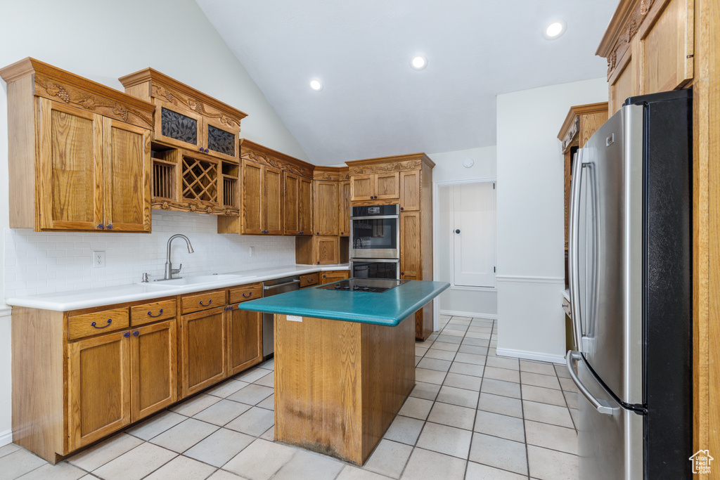 Kitchen with appliances with stainless steel finishes, light tile patterned floors, decorative backsplash, a center island, and vaulted ceiling