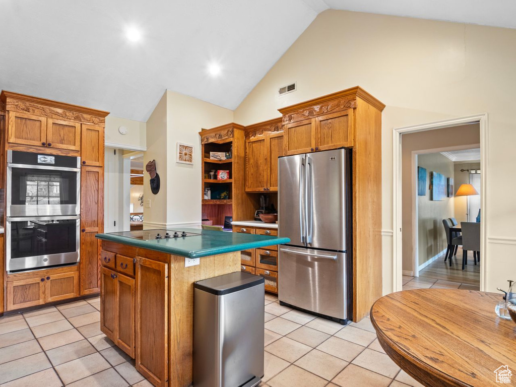 Kitchen featuring appliances with stainless steel finishes, open shelves, a kitchen island, light tile patterned floors, and brown cabinetry