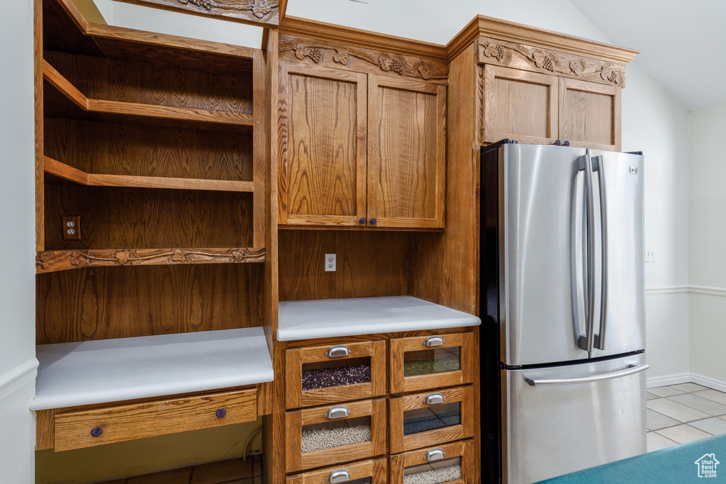 Kitchen featuring freestanding refrigerator, lofted ceiling, light tile patterned floors, brown cabinets, and light countertops