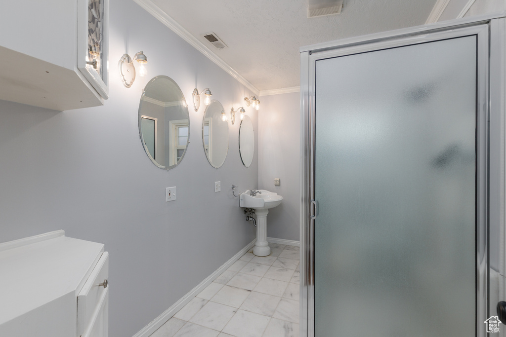 Full bathroom with marble finish floors, crown molding, and a shower stall