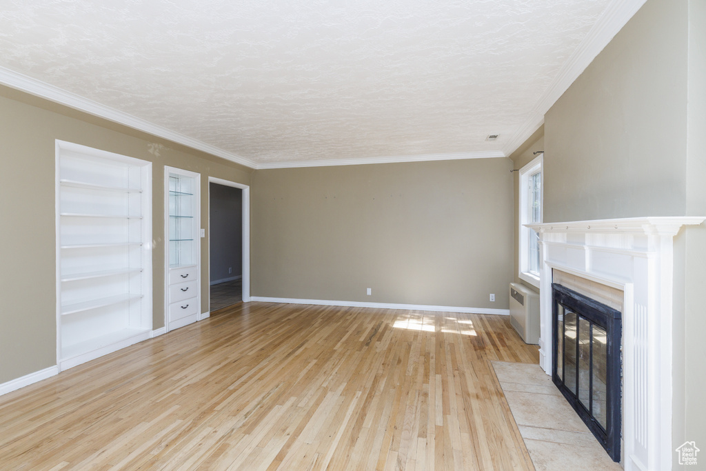 Unfurnished living room featuring light wood-style flooring, a fireplace with flush hearth, crown molding, and built in features