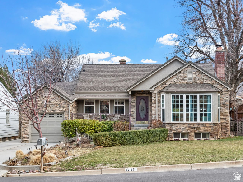 View of front of home with stone siding, concrete driveway, an attached garage, and a front lawn