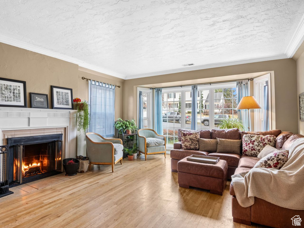 Living area featuring wood finished floors, a textured ceiling, a warm lit fireplace, and crown molding