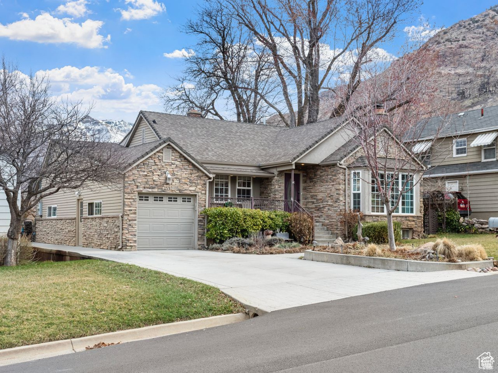 View of front of property featuring stone siding, driveway, an attached garage, a front yard, and roof with shingles