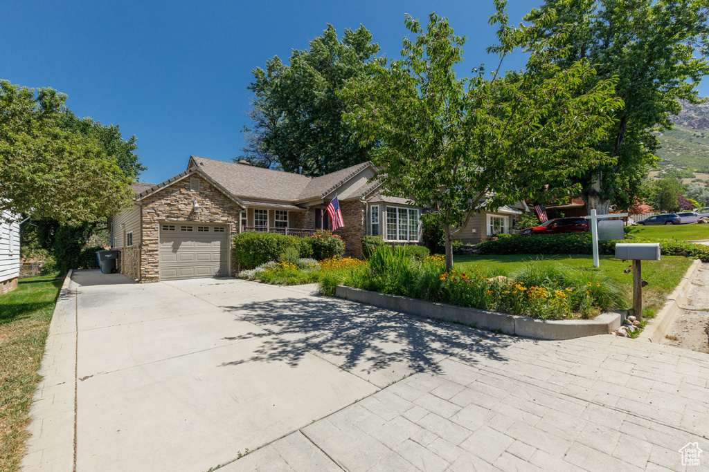 Ranch-style house featuring an attached garage, stone siding, driveway, and a front yard