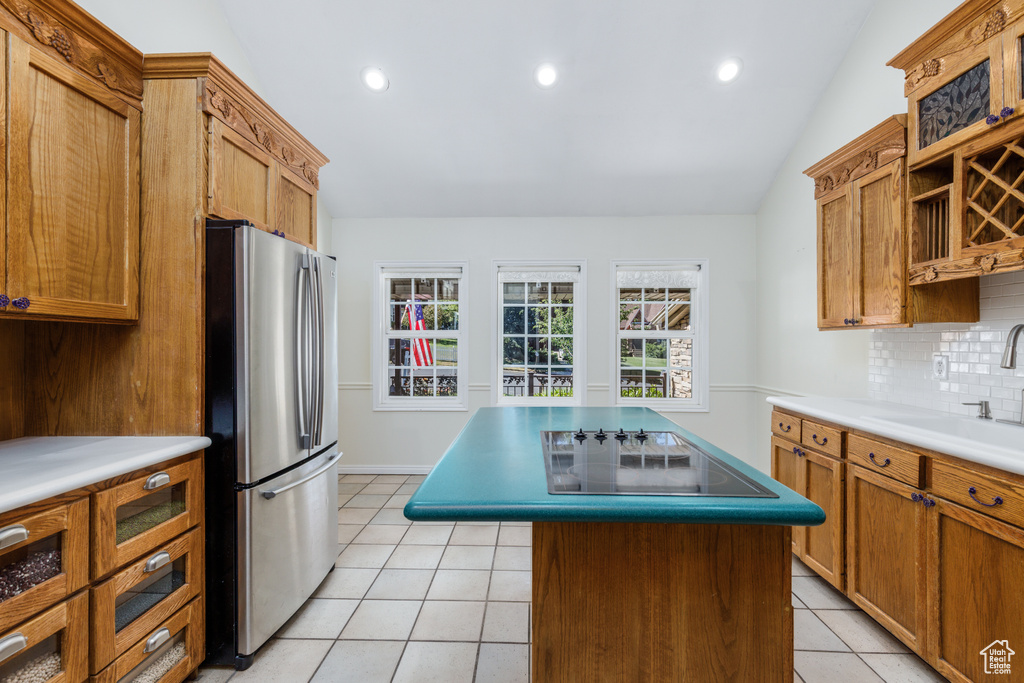 Kitchen with freestanding refrigerator, tasteful backsplash, black electric stovetop, light tile patterned floors, and vaulted ceiling