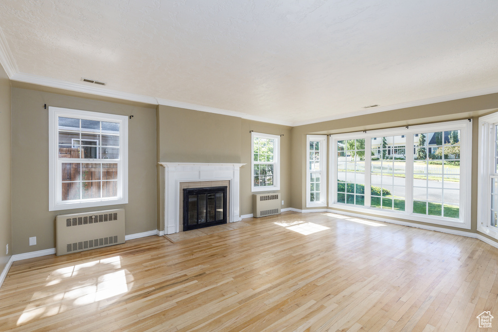 Unfurnished living room with radiator heating unit, ornamental molding, wood finished floors, and a fireplace with flush hearth