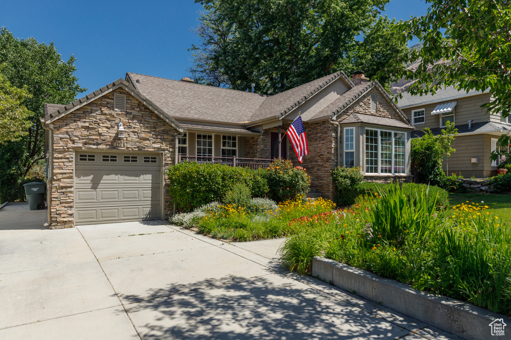 Ranch-style home with a garage, concrete driveway, stone siding, and a chimney