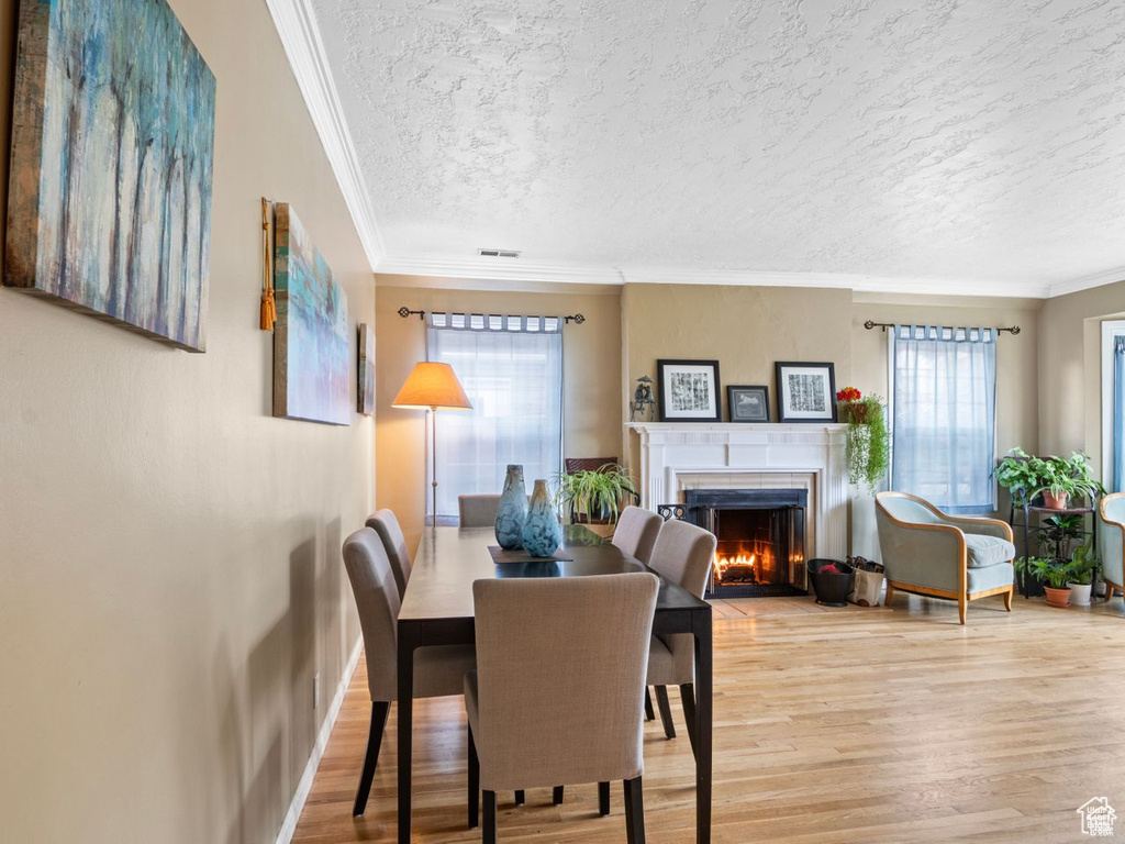 Dining area featuring a lit fireplace, a textured ceiling, wood finished floors, and crown molding