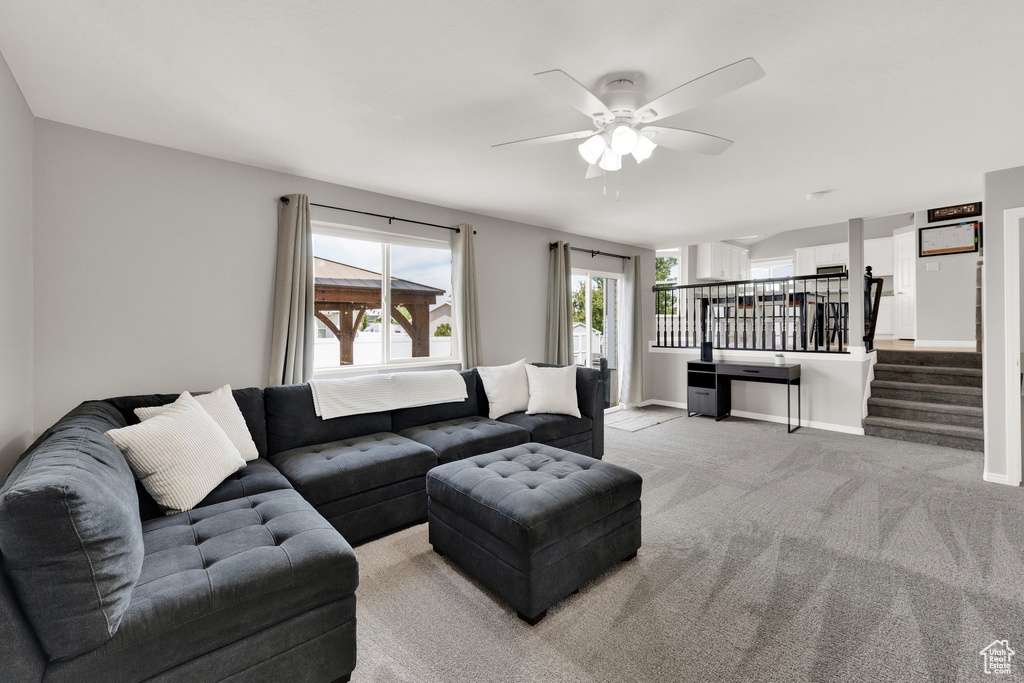 Living area featuring a ceiling fan, light carpet, and stairway