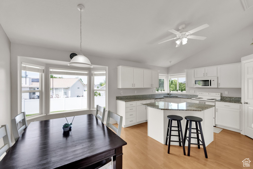 Kitchen featuring white appliances, a breakfast bar area, a kitchen island, ceiling fan, and white cabinetry