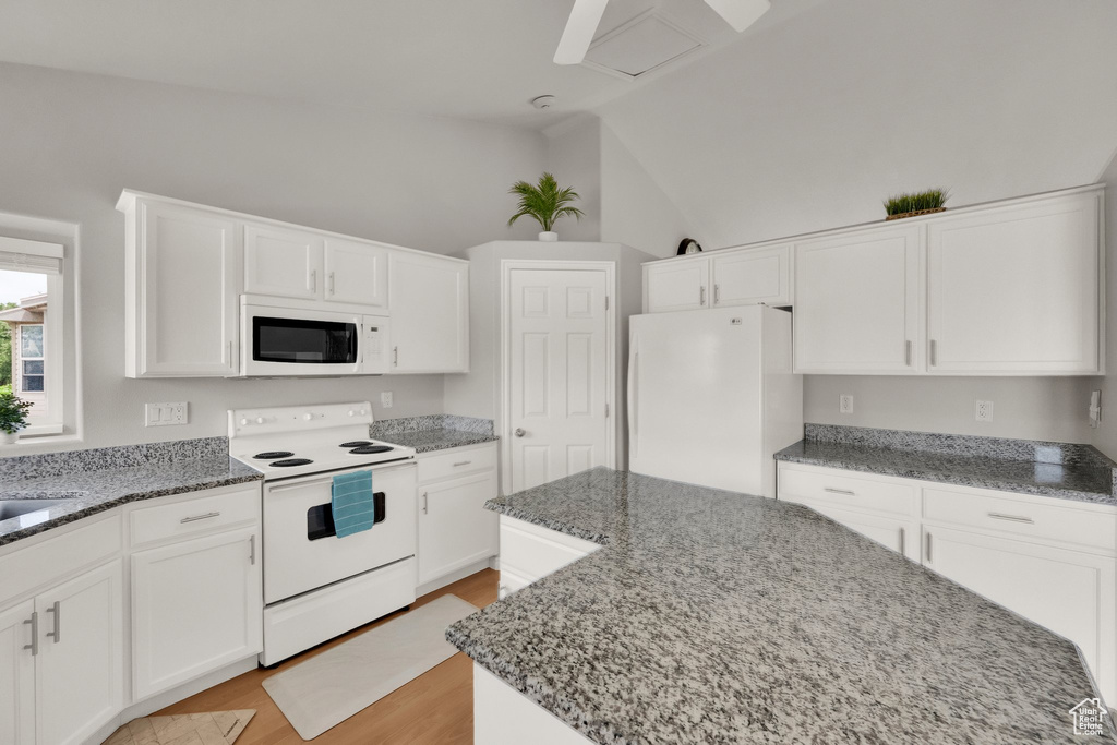 Kitchen featuring white appliances, stone counters, white cabinets, lofted ceiling, and light wood finished floors