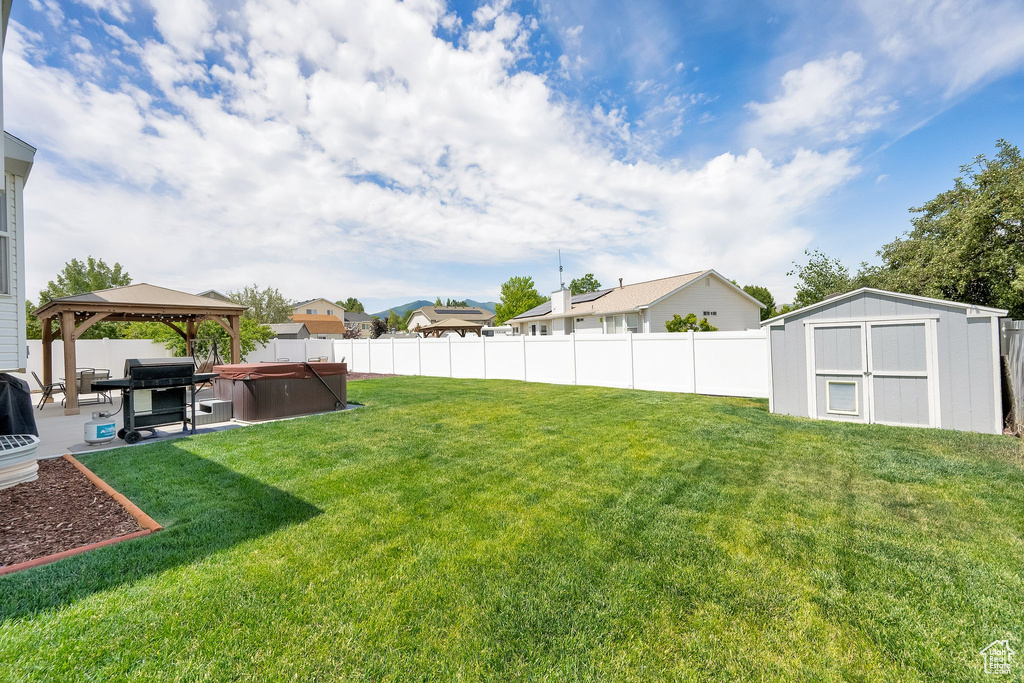Fenced backyard with a hot tub, a shed, a patio area, a gazebo, and a residential view