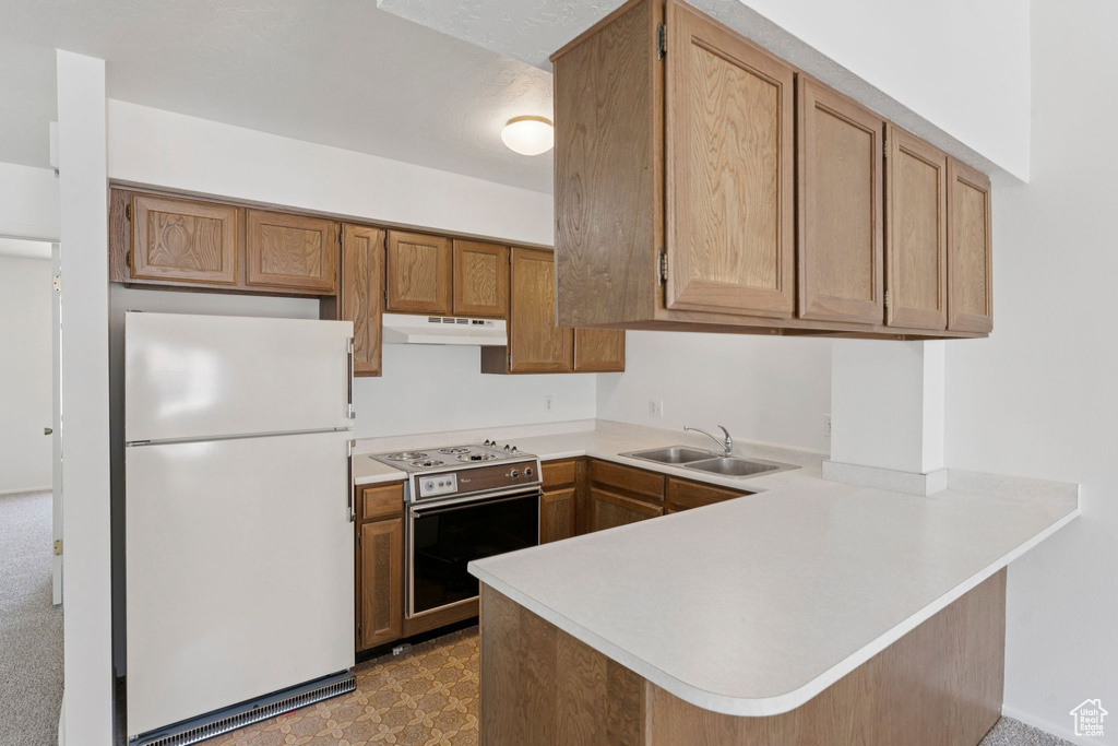 Kitchen with freestanding refrigerator, stainless steel electric range, under cabinet range hood, a peninsula, and light countertops