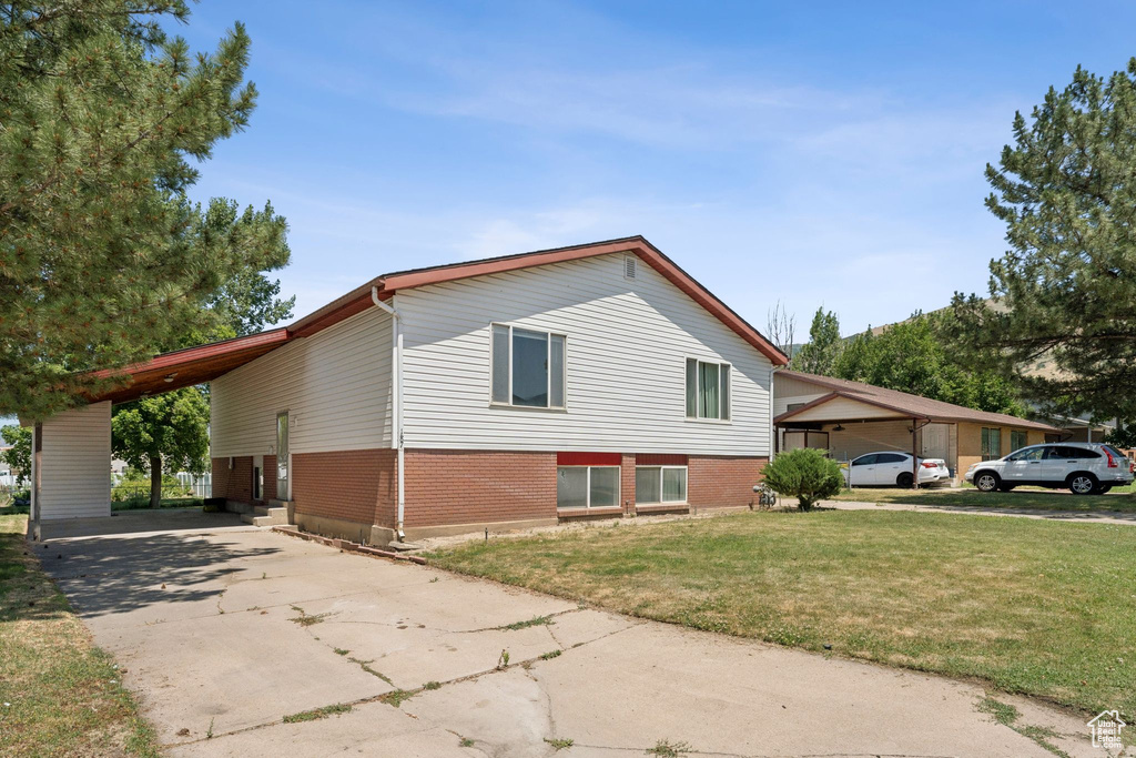 View of property exterior with brick siding, concrete driveway, an attached carport, and a lawn