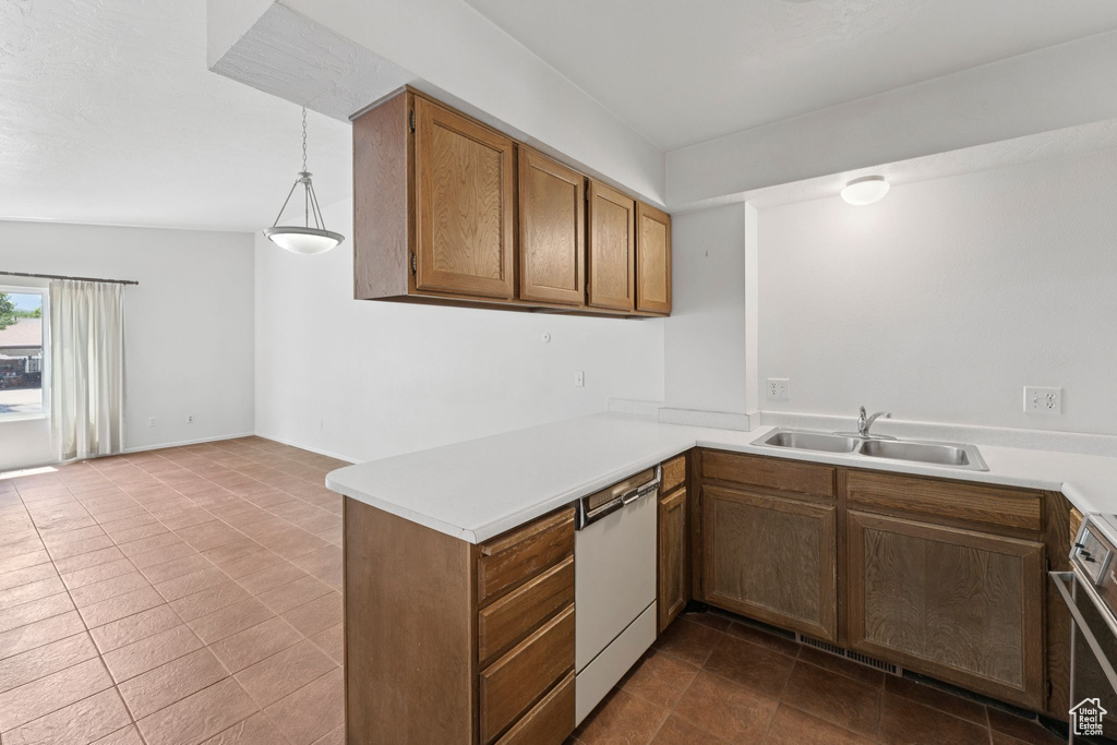 Kitchen with white dishwasher, stove, light countertops, a peninsula, and brown cabinets