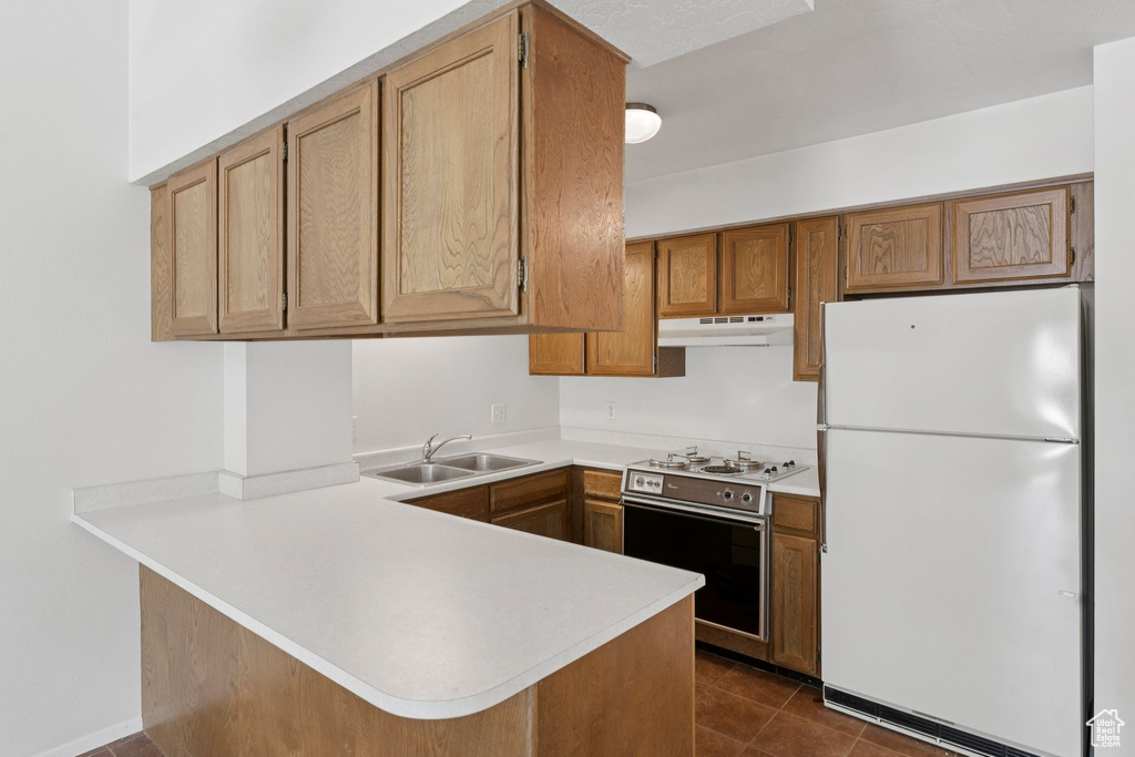 Kitchen featuring freestanding refrigerator, under cabinet range hood, stainless steel range, a peninsula, and light countertops