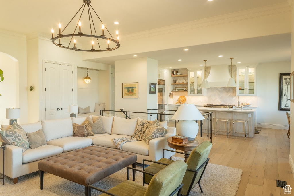 Living area with crown molding, arched walkways, recessed lighting, light wood finished floors, and a chandelier