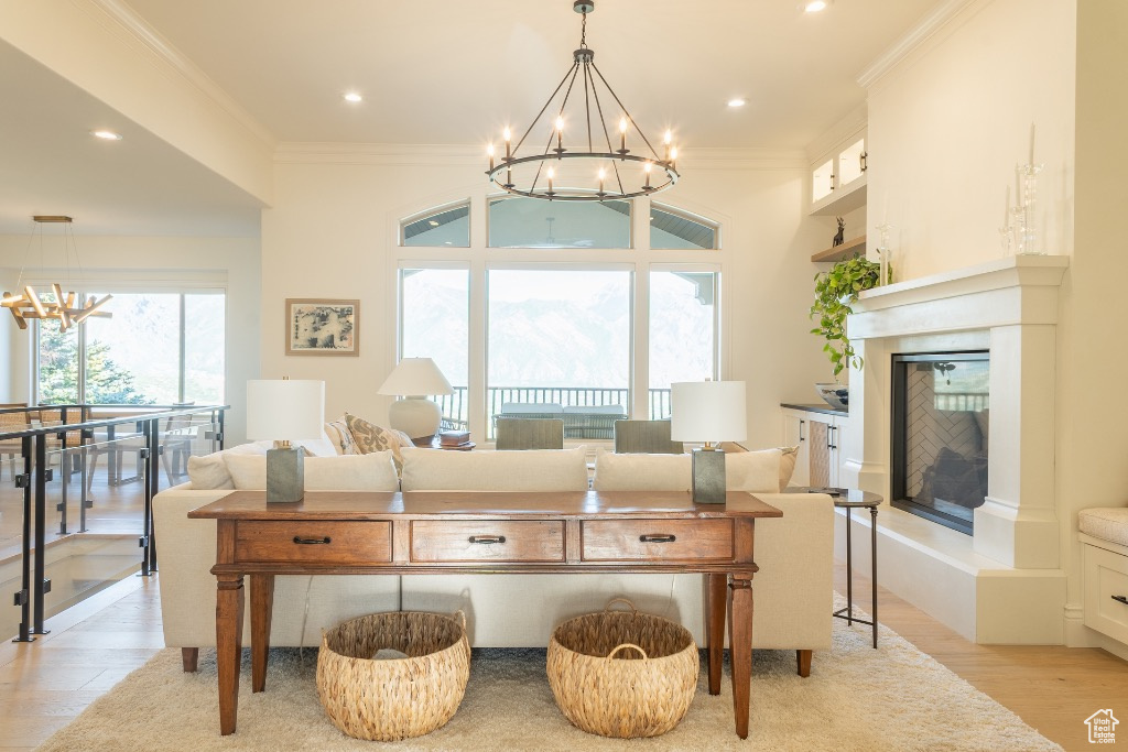 Living room with a chandelier, ornamental molding, a fireplace with raised hearth, light wood finished floors, and recessed lighting