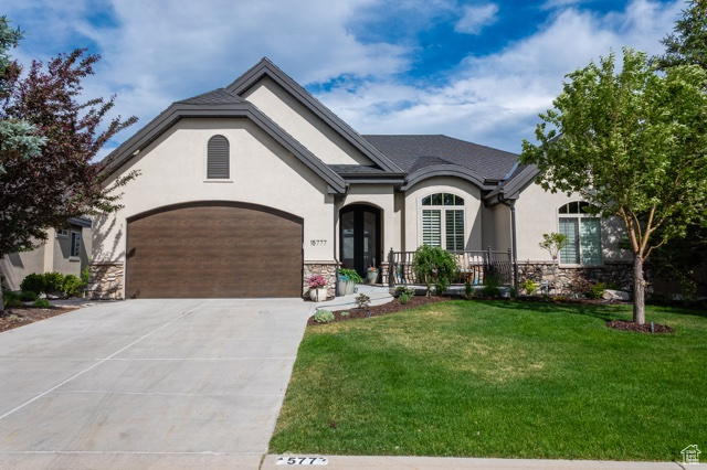 French country style house with stone siding, stucco siding, driveway, a front yard, and a garage