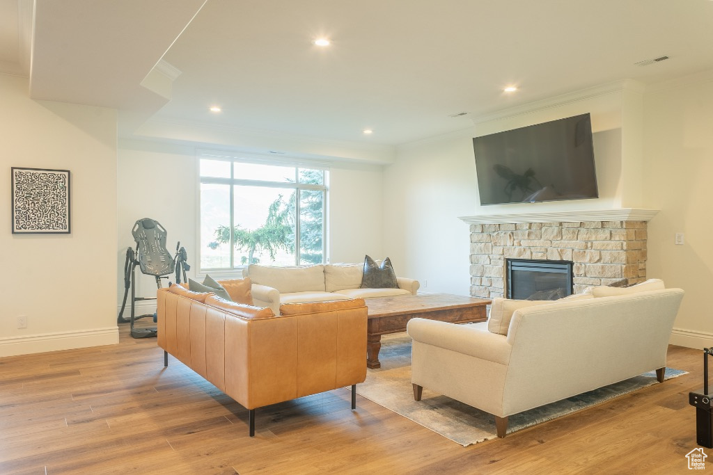 Living room with crown molding, recessed lighting, light wood-style floors, and a fireplace