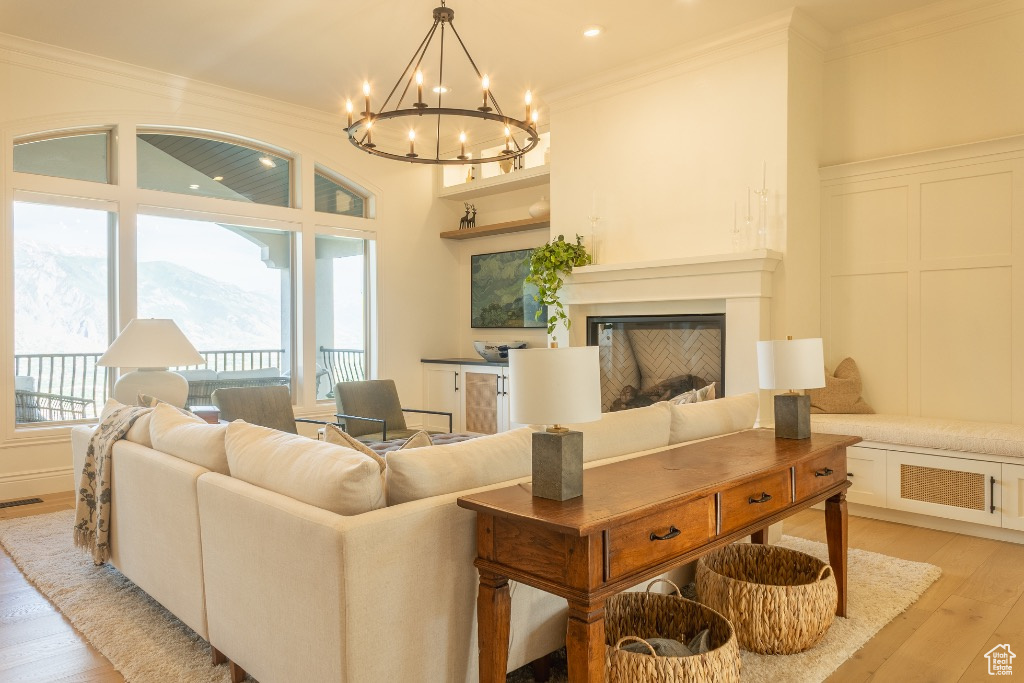 Living room with a chandelier, ornamental molding, light wood-style floors, a glass covered fireplace, and recessed lighting