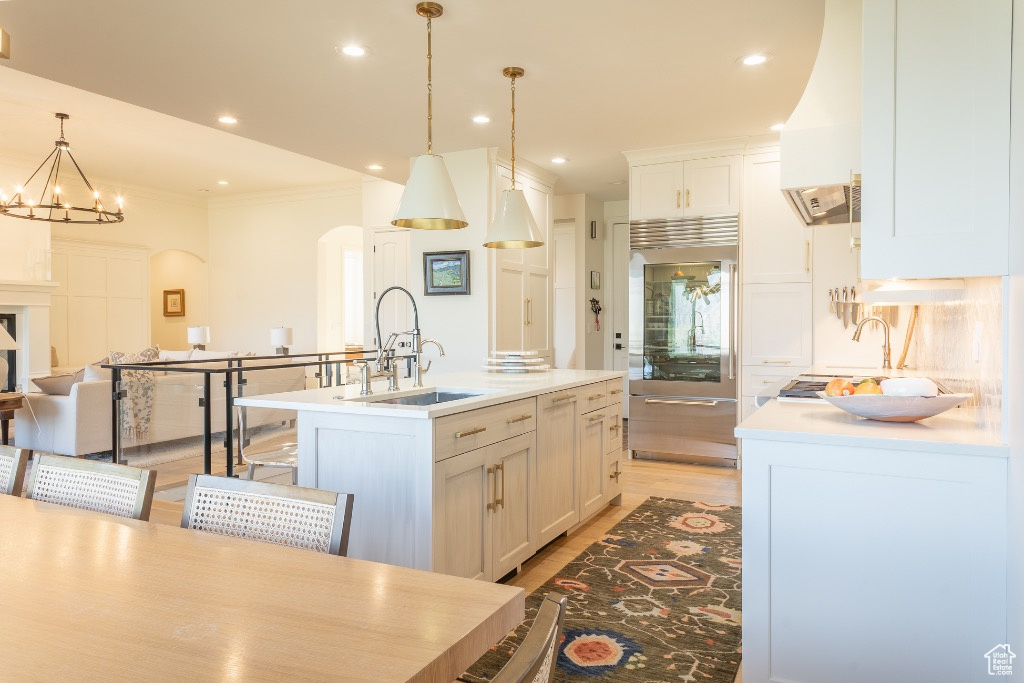 Kitchen with stainless steel built in refrigerator, arched walkways, light wood-style floors, light countertops, and a kitchen island with sink